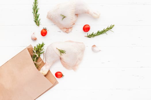 Creative Top view flat lay of fresh raw chicken legs with rosemary herbs garlic tomatoes on white wooden background with copy space. Food preparation recipe cooking concept