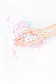 Pearl pastel confetti sparkles with woman hand on white background. Creative conceptual top view flat lay backdrop for your blog, text or design
