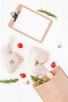 Creative Top view flat lay of fresh raw chicken legs with rosemary herbs garlic tomatoes on white wooden background with copy space. Food preparation recipe cooking concept