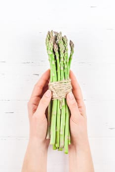 Creative scandinavian style flat lay top view of fresh green asparagus in woman hands on white wooden table background copy space. Minimal house cooking concept for blog or recipe book