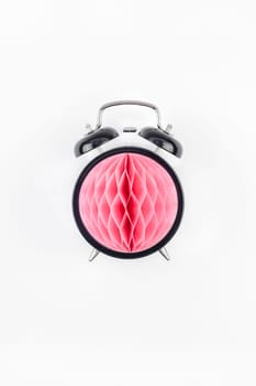Birthday or baby shower party invitation card template. Black alarm clock with pink honeycomb paper ball on white background. Creative conceptual top view flat lay composition in minimal style