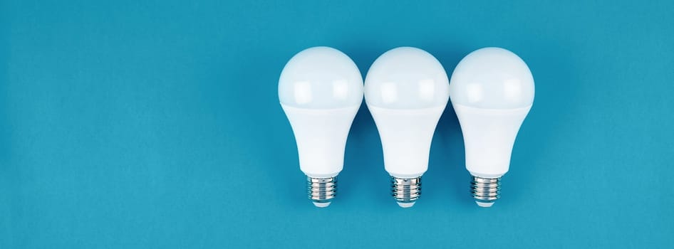 Energy-saving and eco-friendly life in conceptual frame pattern. Creative top view flat lay of LED light bulbs composition with copy space on blue background in minimal style.