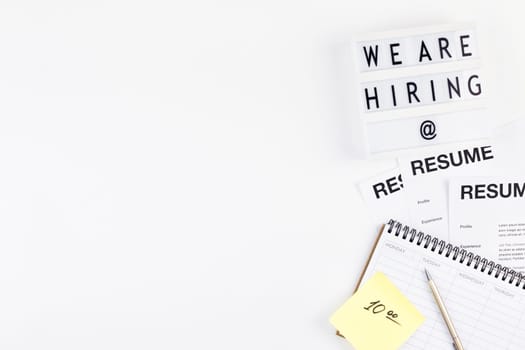 Creative top view flat lay of desk with we are hiring text on lightbox with copy space on white background in minimal style. Concept of new job, hiring recruitment process, new team members screening