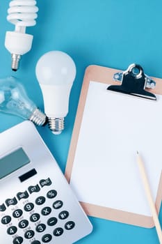 Energy and money saving and eco-friendly life in conceptual composition. Creative top view flat lay of new and old light bulbs calculator and clipboard with copy space on blue background minimal style