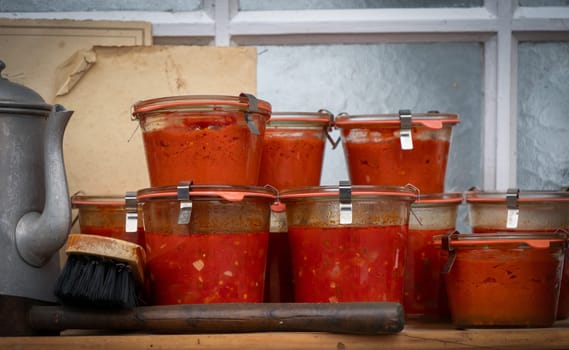 A row of glass jars filled with red sauce sit on a wooden table. The jars are of various sizes and are arranged in a neat row. Concept of abundance and abundance of food
