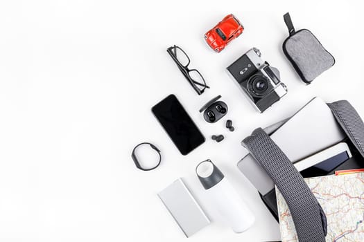 Creative top view flat lay of open backpack with laptop and tablet inside, mobile phone map copy space white background minimal style. Concept of modern man accessories for travel adventures and life