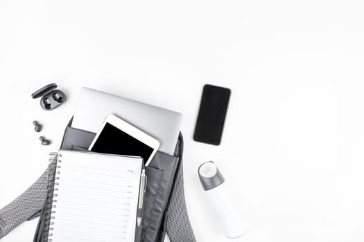 Creative top view flat lay of open backpack with laptop and tablet inside, mobile phone, copy space white background minimal style. Concept of modern man accessories for education, business and life
