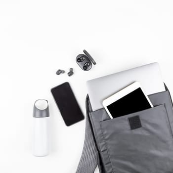 Creative top view flat lay of open backpack with laptop and tablet inside, mobile phone, copy space white background minimal style. Concept of modern man accessories for education, business and life