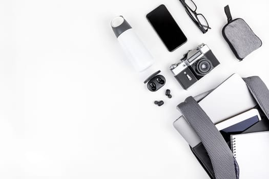 Creative top view flat lay of open backpack with laptop and tablet inside, mobile phone, copy space white background minimal style. Concept of modern man accessories for education, business and life