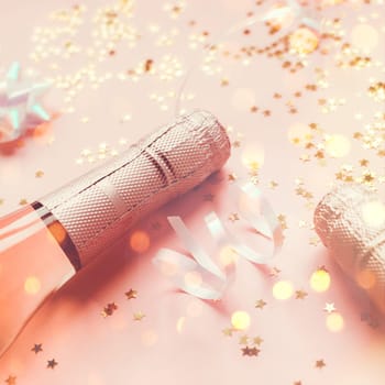 Christmas or New Year composition with bottles of rose champagne and golden shiny sparkle star confetti on pastel pink background, side view. Party Celebration creative concept