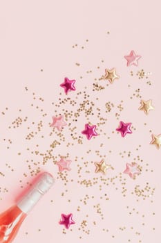 Christmas or New Year composition with bottles of rose champagne and golden shiny sparkle star confetti on pastel pink background, top view. Celebration flat lay. Party creative concept