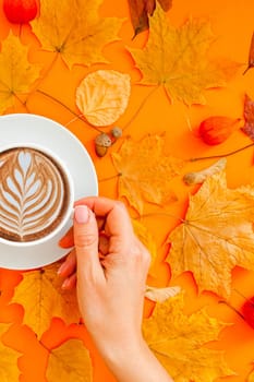 Autumn flat lay composition with dry leaves wreath frame and coffee latte cup in woman hand on bold orange color background. Creative autumn thanksgiving, fall, halloween concept. Top view, copy space