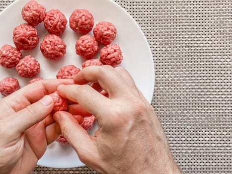 Man hands preparing meatballs with raw mincemeat. Lifestyle close up composition with natural light. Homemade cooking during lockdown, stay home housekeeping sharing concept. Top view with copy space