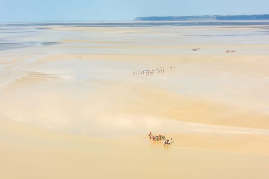 View from walls of Mont Saint Michel on the bay during the low tide with groups of tourists walking. France