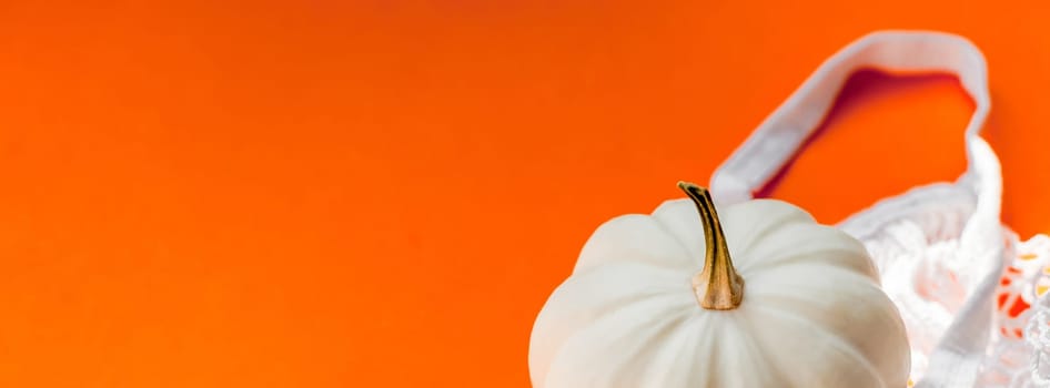 Autumn flat lay composition with white pumpkins in mesh shopping bag on bold orange color background. Creative autumn, thanksgiving, fall, halloween concept in zero waste style. Top view, copy space