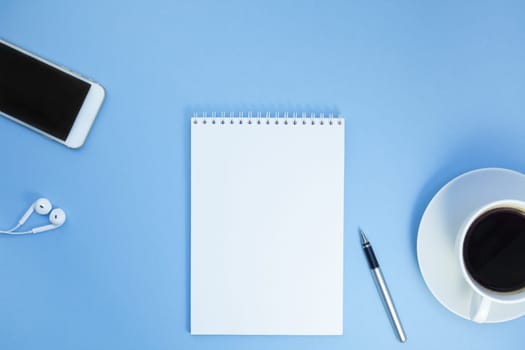 Creative flat lay photo of workspace desk with paper notebook, smartphone, earpieces, pen and coffee with copy space background minimal style