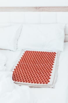 Acupuncture mat in bed. Wellness, reflexology and self care treatment at home concept. Alternative therapy massager with acupressure points. Reduce muscle tension, back pain, improve blood circulation