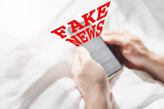 Fake news infodemics during Covid-19 pandemic concept. Man hands holding mobile phone reading global news or social net at home. Reading last news update in lockdown. Red text fake news on foreground