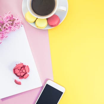 Creative flat lay photo of coffee cup with macaroons and a notepad with copy space on pink and yellow background minimal style