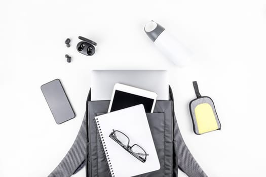 Creative top view flat lay of open backpack with laptop and tablet inside, mobile phone, copy space white background minimal style. Concept of modern man accessories for education, business and life