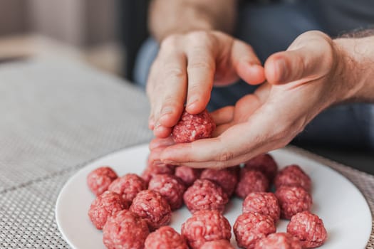 Man hands preparing meatballs with raw mincemeat. Lifestyle close up composition with natural light. Homemade cooking during lockdown, stay home housekeeping sharing concept. Side view with copy space