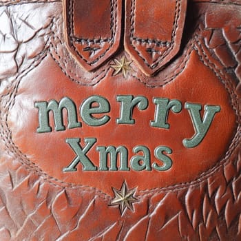 A beautifully crafted leather bag displays a festive merry Xmas message surrounded by decorative stars in vibrant colors.