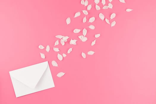 Creative flat lay concept top view of blank letter mock up and apple tree flowers petals on pastel pink background with copy space in minimal style, template for text