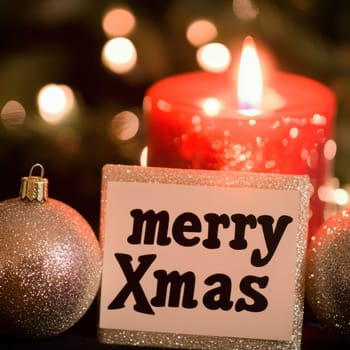 A festive card wishes Merry Christmas near a lit red candle with sparkling ornaments creating a warm holiday atmosphere.