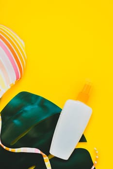 Tropical jungle palm monstera leaves, sunglasses, sunscreen blank bottle mockup and woman's swimsuit top on bright yellow paper background. Summer vacations creative flat lay concept template for text