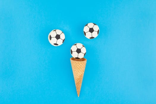 Creative flat lay top view of ice cream waffle cones with soccer balls macarons on bright bold blue background with copy space in minimal style, concept of football games for children birthday