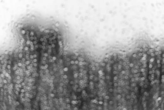 Rain water drops on a window glass surface. Defocused bw blur image with bokeh
