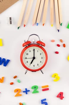 Creative flat lay back to school concept with alarm clock, color school and office supplies on white table background with copy space, frame, template for text or design