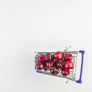 Square top view of ripe cherries in a shopping cart with copy space isolated on white background in minimal style. Concept of supermarket or fruit market shopping. Template for your text or design.