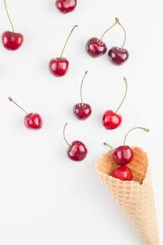 Creative top view of ripe cherries in a waffle cone with copy space isolated on white background in minimal style. Concept of summer fun and healthy eating. Template for your text or design.