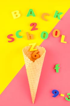 Creative flat lay back to school concept with waffle cone and welcome letters message on bright yellow and pink paper background with copy space, template for text or design