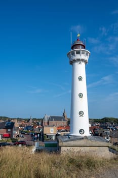 The approx. 28 m high white lighthouse J.C.J. van Speijk in Egmond aan Zee, North Holland, Netherlands with some of the town's houses
