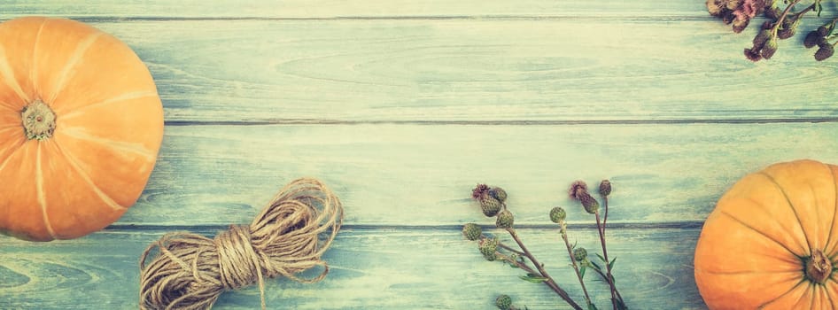 Top view of autumn orange pumpkins and dry flowers and grass thanksgiving background over blue toned wooden table with copy space. Template for fall harvest mood text. Long wide banner