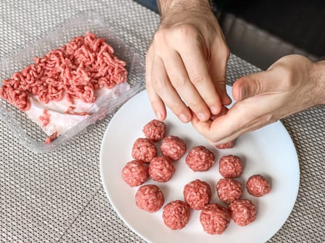 Man hands preparing meatballs with raw mincemeat. Lifestyle close up composition with natural light. Homemade cooking during lockdown, stay home housekeeping sharing concept. Above view