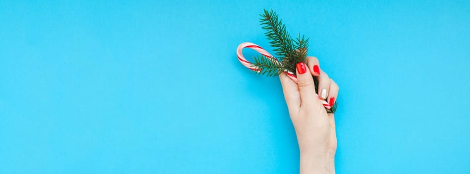 New Year or Christmas top view Xmas holiday celebration woman hand red manicure holding fir branch sweet cane copy space turquoise blue color paper background minimal style. Long wide banner