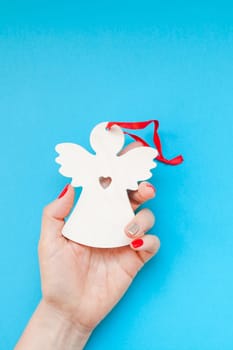 New Year or Christmas top view Xmas holiday celebration woman hand red manicure holding homemade wooden angel toy copy space turquoise blue color paper background minimal style. Template greeting card