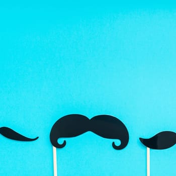 Creative square flatlay overhead top view retro black paper photo booth props moustaches turquoise background copy space. Men health awareness month fathers day masculinity concept blog social media