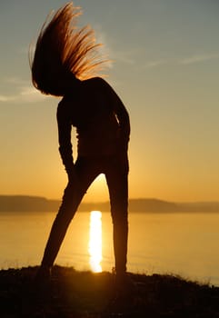 A captivating silhouette of a woman with her flowing hair blowing in the wind during a picturesque sunset