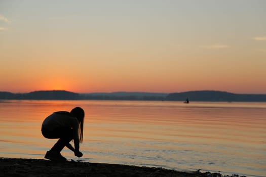 A serene silhouette of an individual peacefully exploring the beautiful shoreline as the sun sets on the horizon