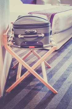 Hotel room with a suitcase on the luggage place and the bed. Filtered shot