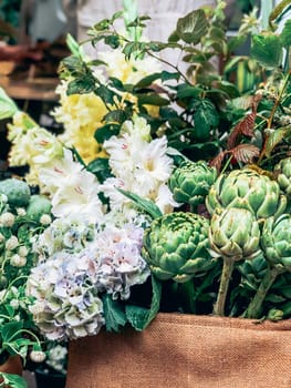 Beautiful fresh decorative green artichokes and other flowers in small florist shop. Modern style flowers arrangement in lifestyle natural light composition. Small business. Mobile photo