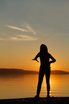 A calm and serene silhouette stands against the vibrant, colorful sunset by the peaceful waters edge