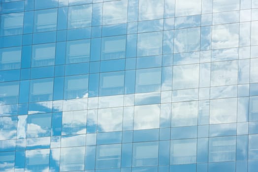 blue sky and clouds reflected in windows of modern office building