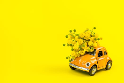 Moscow, Russia - February 23, 2019: 8 March International Women's Day card with toy model of retro car delivering bouquet of mimosa flowers on yellow background. Valentine's day, Flower delivery concept