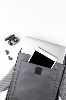 Creative top view flat lay of open backpack with laptop and tablet inside, mobile phone, copy space white background minimal style. Concept of modern man accessories for education, business and life