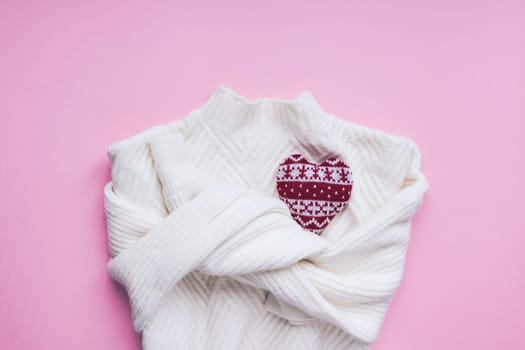 Creative valentine's day romantic flat lay overhead top view white sweater and knitted heart pink background copy space minimal style with natural light. 14 February holiday template for feminine blog